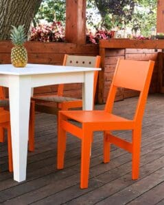 A bright orange chair next to a white table on a wooden patio, with a pineapple as a centerpiece.