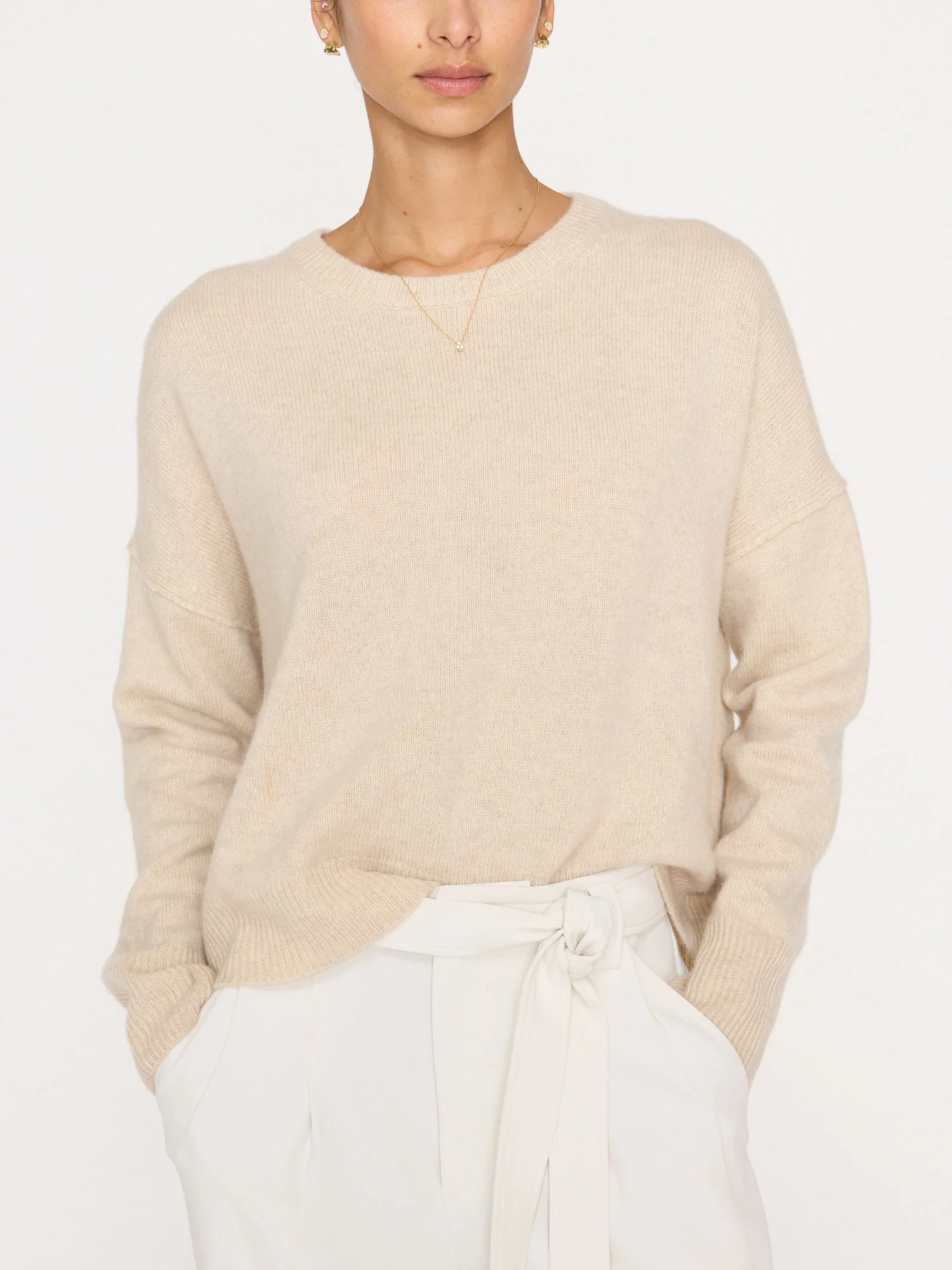 A woman wearing a soft oatmeal-colored cashmere sweater with a relaxed fit and long sleeves, paired with light-colored trousers.