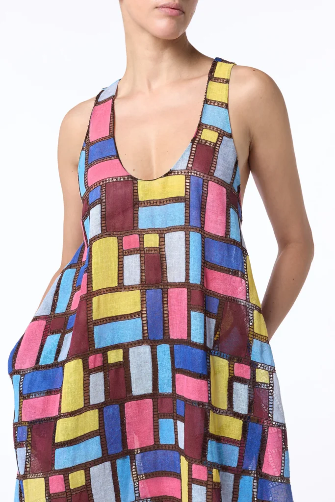 A model showcasing a colorful Gabriela Hearst patchwork midi dress featuring geometric patterns in blue, pink, yellow, and brown hues.