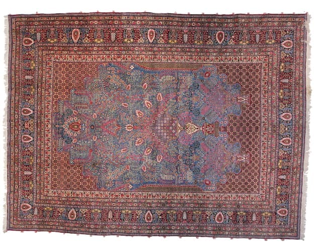 A vintage rug featuring intricate floral patterns in rich tones of pink, orange, and blue, with a central medallion and an ornate border.
