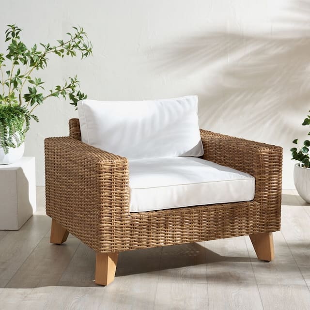 A modern outdoor chair made of woven rattan with a white cushion, set against a light background and surrounded by indoor plants.