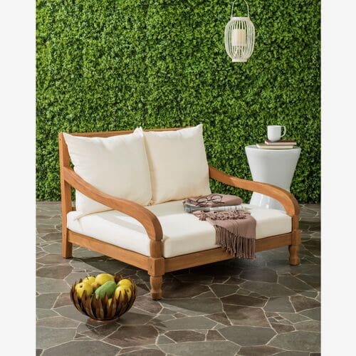 Cozy outdoor lounge chair with cream cushions, nestled against a green hedge backdrop, accompanied by a small side table and decorative items.