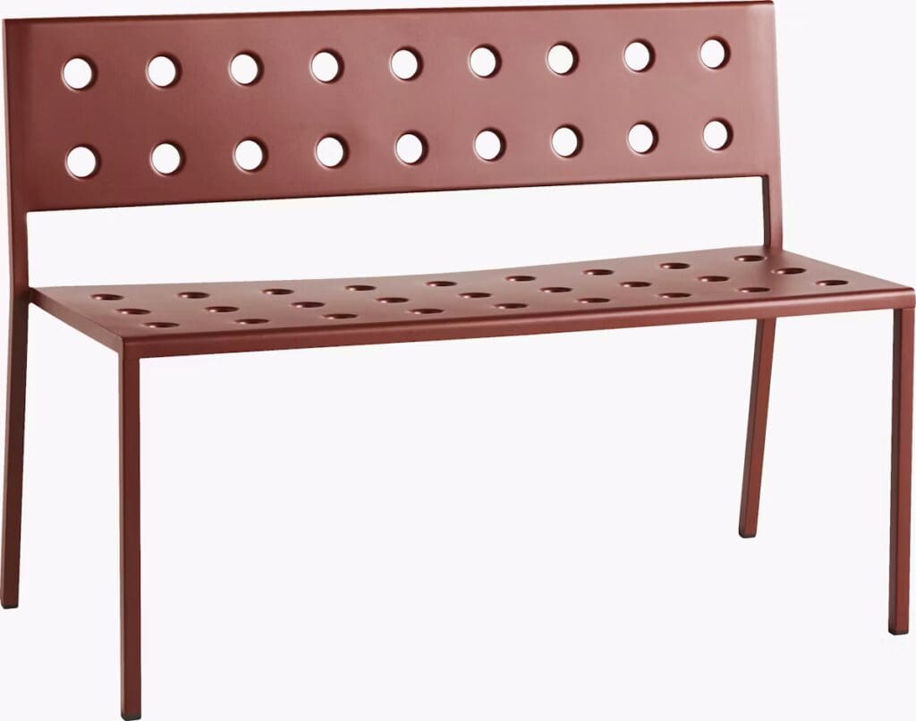 A modern metal bench in a reddish-brown color featuring circular cutouts along the seat and backrest, supported by slim legs.