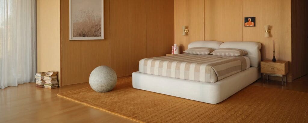 A modern bedroom featuring a striped bedspread on a low-profile bed, with wooden paneling, a small bedside table, and a rounded decorative object on the floor.