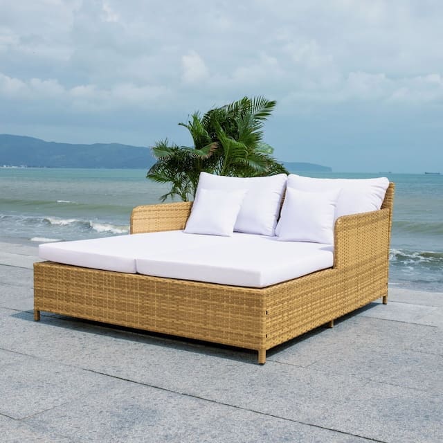 Modern outdoor daybed with white cushions set against a tropical ocean backdrop, featuring a palm plant on one side.