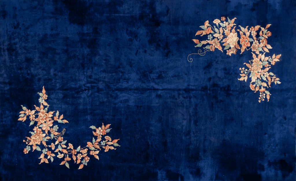 Antique rug featuring a deep navy background adorned with intricate floral patterns in soft orange and green tones, enhancing its vintage charm.