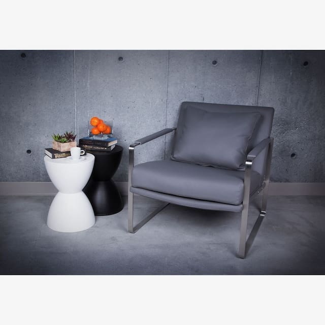 Modern gray lounge chair with a sleek metal frame and cushion, next to a black and white side table holding a small plant, books, and a cup.