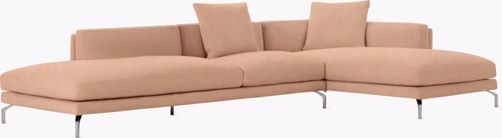 A modern sectional sofa in a light peach color, featuring clean lines and two back cushions. The sofa is supported by sleek metal legs.