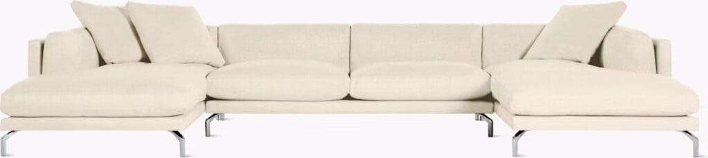 A modern, light-colored sectional sofa with plush cushions and several decorative pillows, featuring a sleek design and chrome legs.