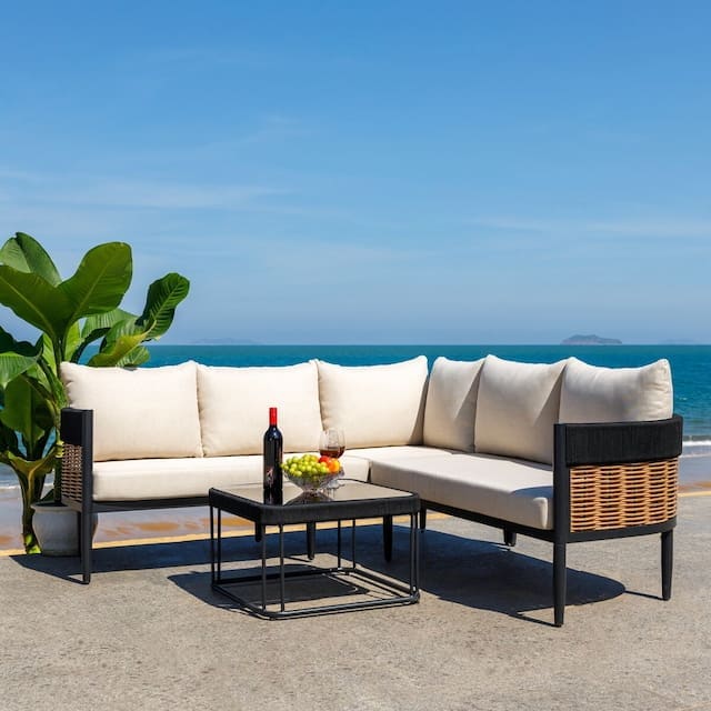 Luxurious outdoor seating area featuring a modern sectional sofa with cream cushions, a black metal coffee table, and a bottle of wine, set against a backdrop of a tropical ocean view and clear blue sky.