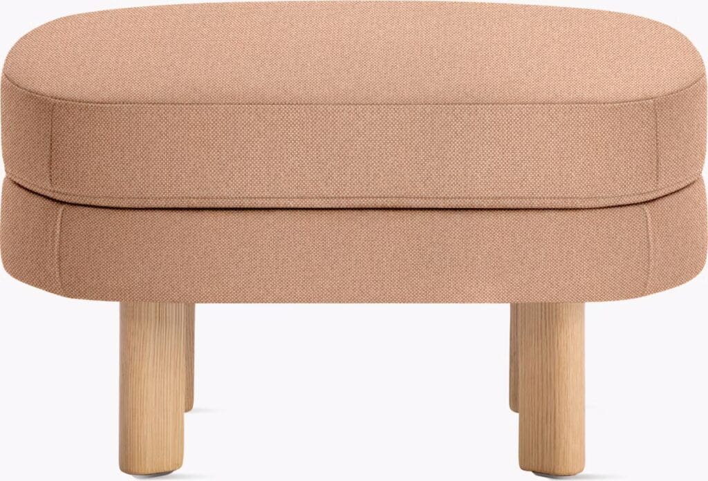 A modern, rounded ottoman in a soft pink fabric, featuring two layered cushions on a light wooden base.