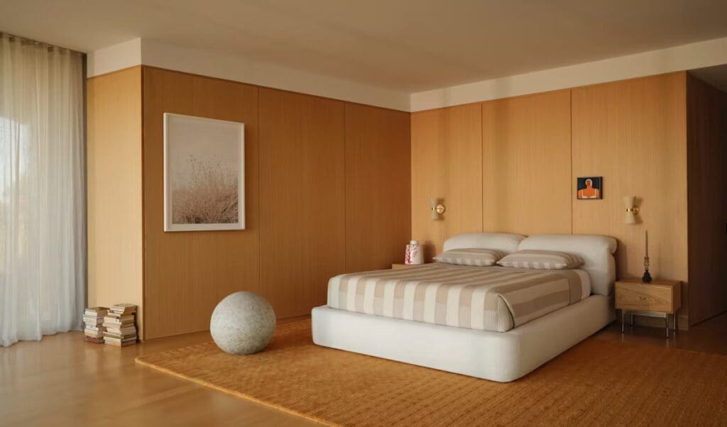 A modern bedroom featuring a low-profile bed with a striped bedspread, wooden paneling, a small bedside table, and a rounded decorative object on the floor.