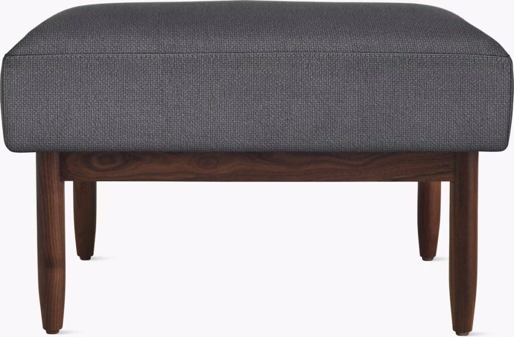 A modern ottoman with a dark gray upholstered top and wooden legs, designed for comfort and style.