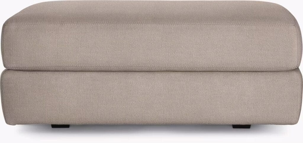 A modern, stylish ottoman in a light gray fabric, featuring a low-profile and clean lines, designed for versatile use in contemporary living spaces.
