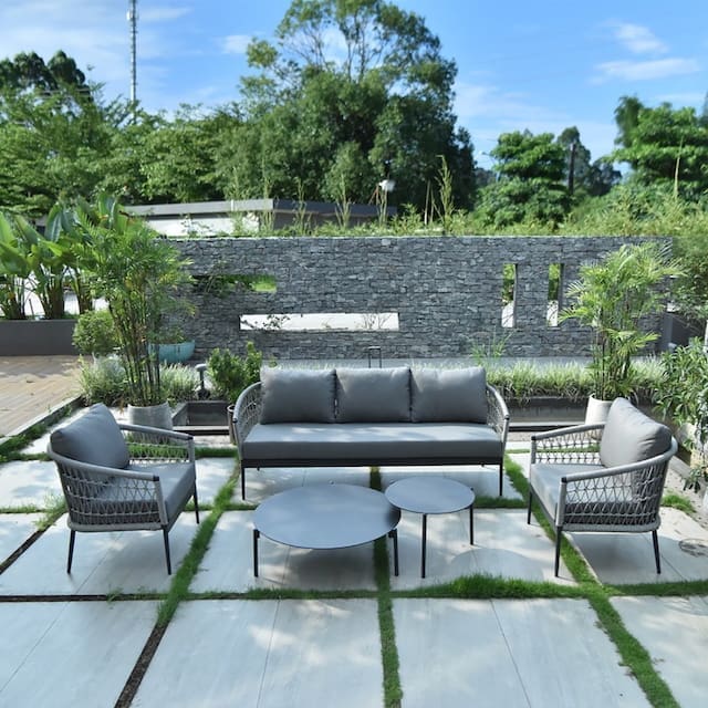 Modern outdoor living space featuring a gray sofa and armchairs with a stone wall backdrop and lush greenery.