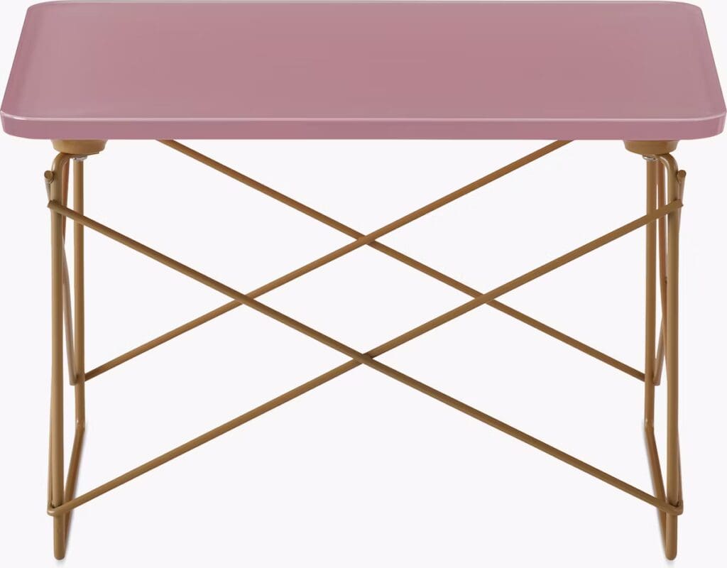 A modern side table featuring a pink top and a crossed metal base in a contrasting gold color.