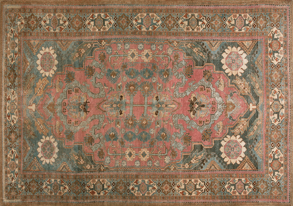 Intricate vintage rug featuring floral patterns in soft pink, orange, and blue tones with a central medallion and ornate border.