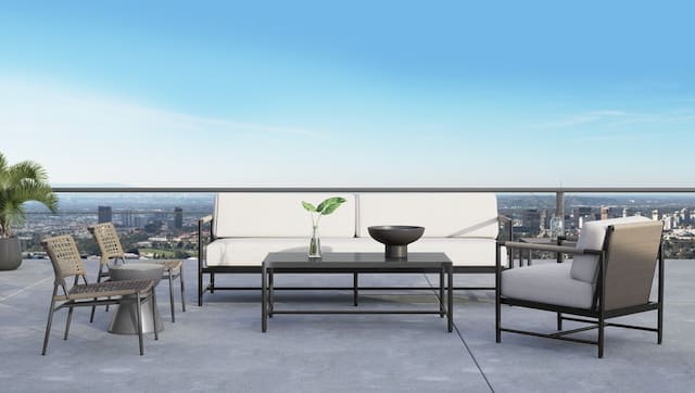 Modern outdoor lounge area on a rooftop terrace featuring stylish furniture, a center table with a plant, and a scenic city view under a clear blue sky.