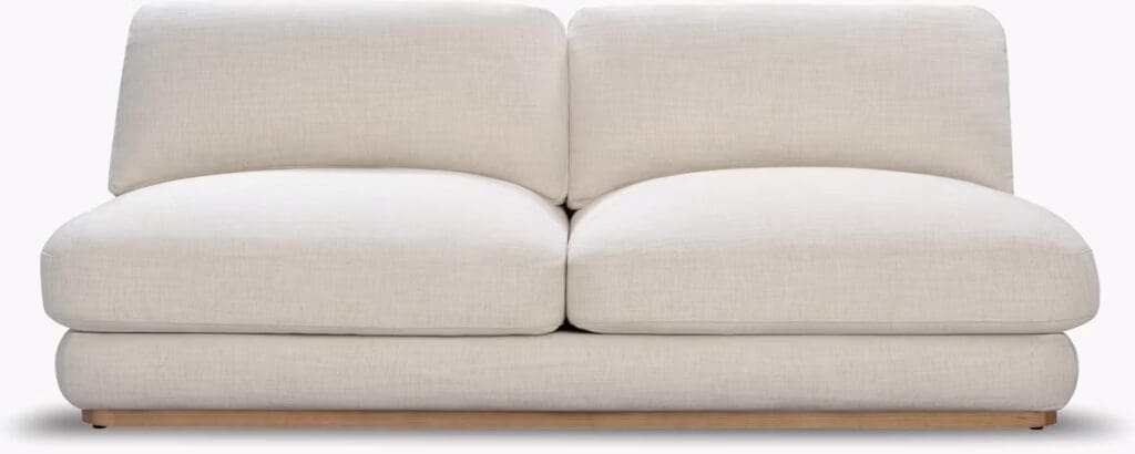 A modern white sofa with a low profile, featuring plush cushions and a simple design, set against a neutral background.