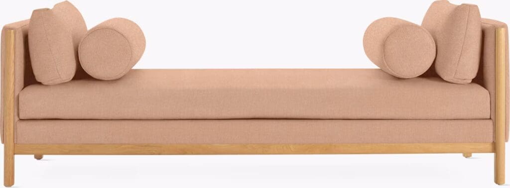 A modern, minimalist daybed with a wooden frame, featuring a light pink upholstered mattress and round cushions for added comfort.