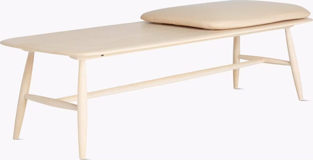 A minimalist low coffee table with a light wooden frame and a soft beige cushion on top.