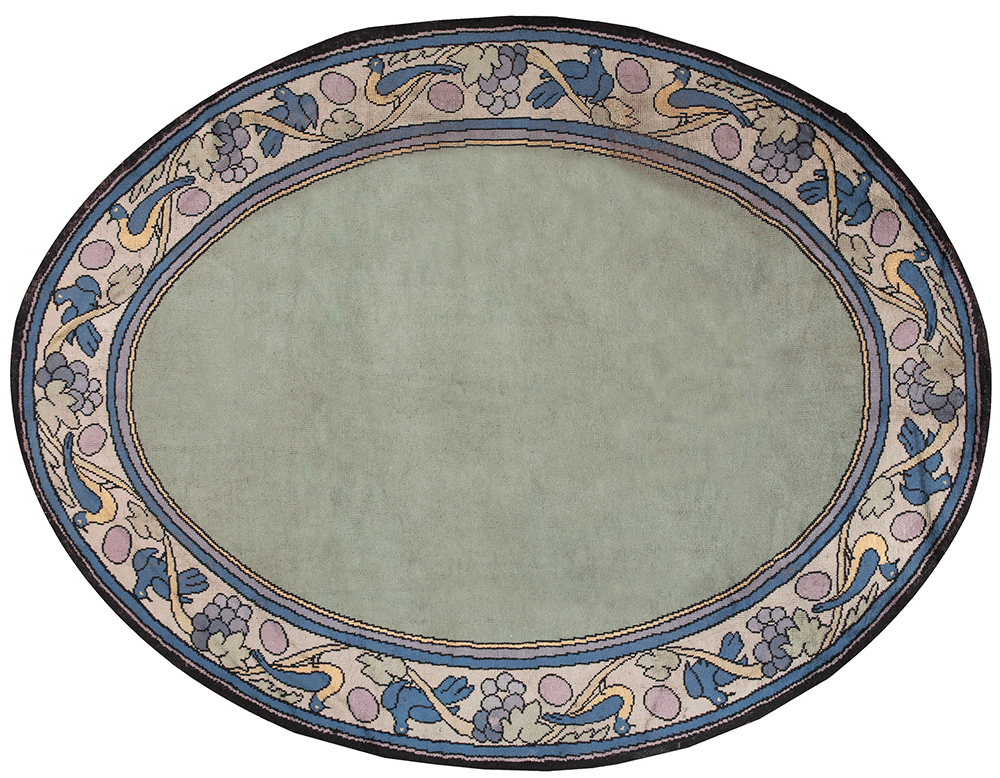An oval vintage rug featuring a soft green center with an intricate floral pattern in soft blue, purple, and beige tones around the border.