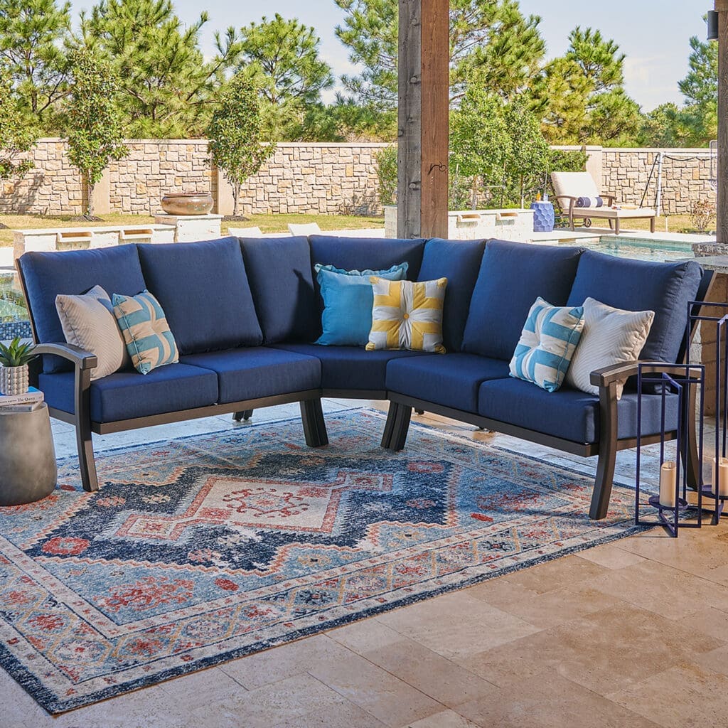 Luxurious outdoor seating area with a navy sectional sofa adorned with colorful cushions, set on a decorative rug beside a pool.