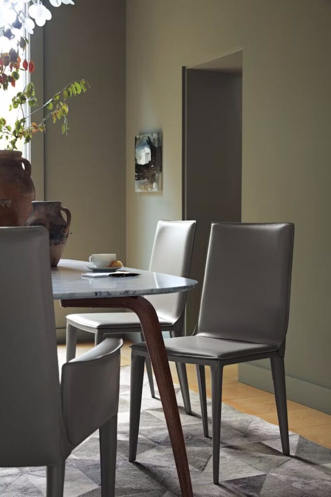 A modern dining area featuring a sleek table with a marble top and elegant chairs, surrounded by a soft rug and natural light from nearby windows.