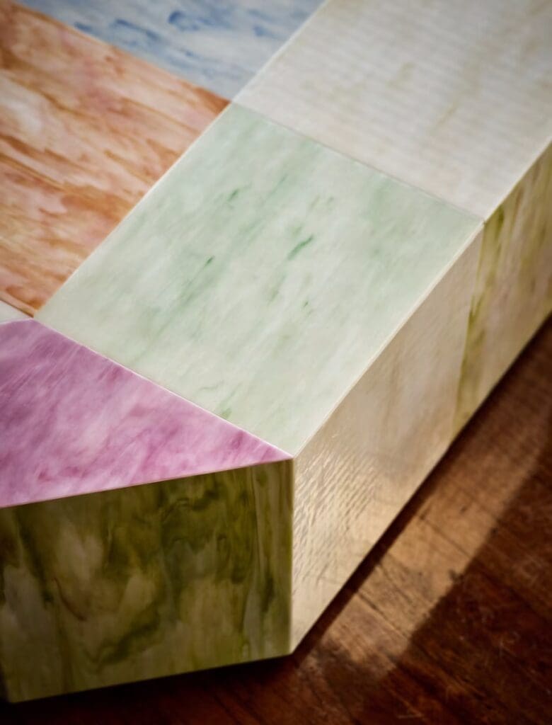 Close-up of a multi-colored, abstract design featuring soft pastels in mint green, pink, and purple, applied to a smooth surface with a wooden base.
