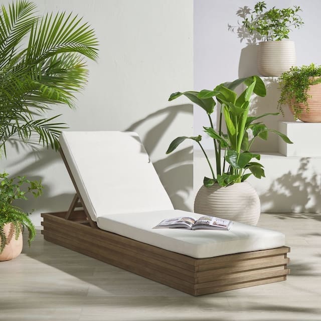 Modern outdoor lounge chair with a white cushion, surrounded by greenery and potted plants, set against a light-colored wall.