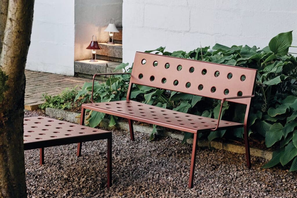 A modern outdoor bench and table set with a dotted design, surrounded by greenery in a garden setting.