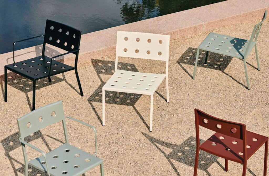 A set of colorful outdoor chairs with circular cutouts, arranged on a sandy surface near a body of water.