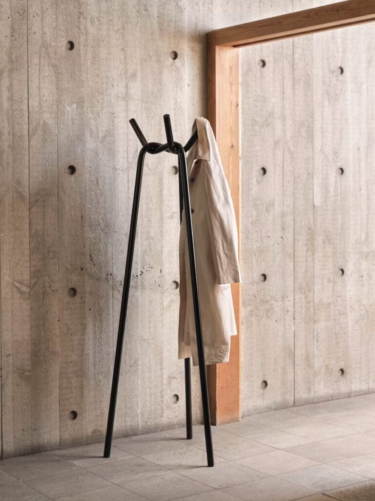 Minimalist black coat rack with a white coat hanging, set against a textured gray concrete wall.