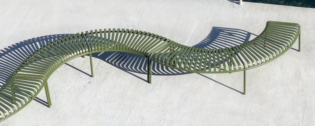 Curved green outdoor bench with slatted design casting shadows on a light surface.