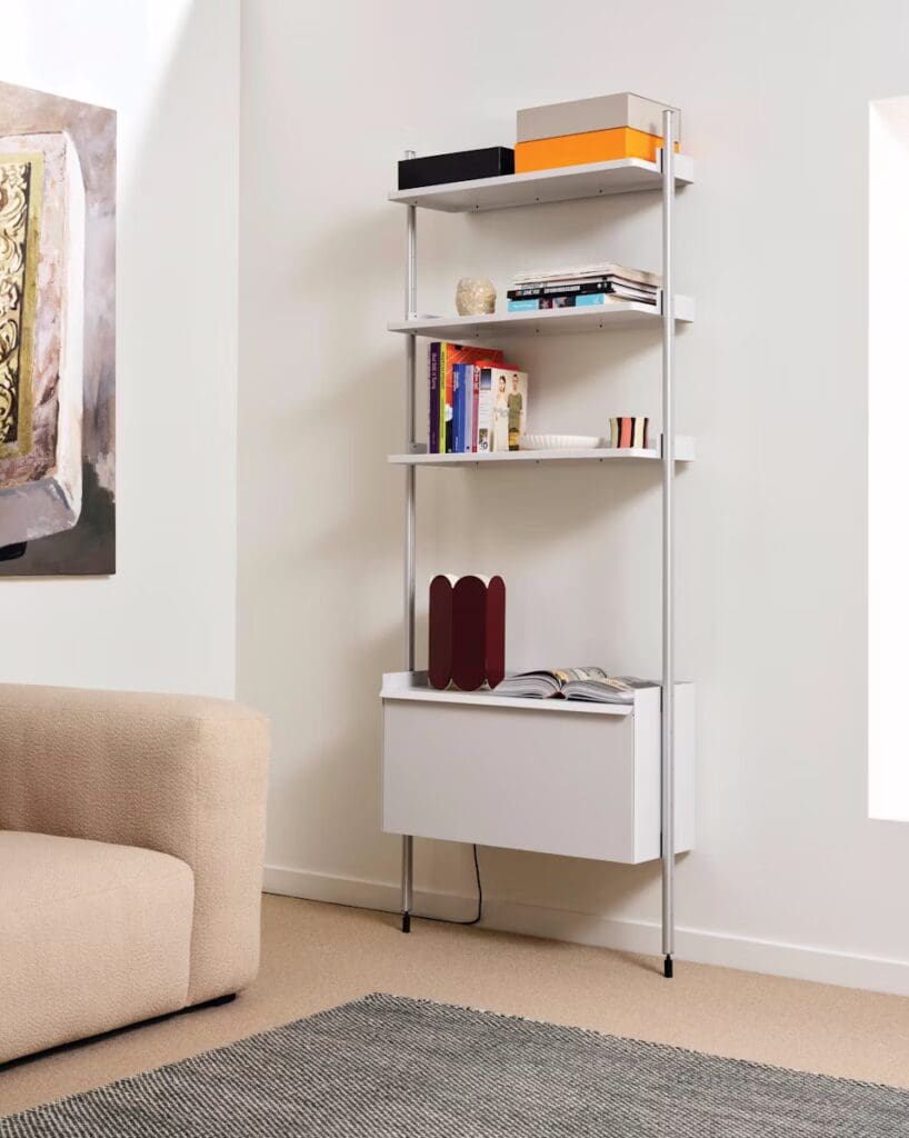 A modern living space featuring a minimalist bookcase with multiple shelves displaying books and decorative items, alongside a plush beige sofa and a textured area rug.
