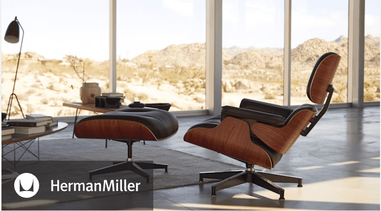 A Herman Miller lounge chair with an ottoman, set against a backdrop of large windows showcasing a desert landscape.