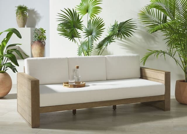 Contemporary outdoor sofa with white cushions and wooden frame, surrounded by potted plants.