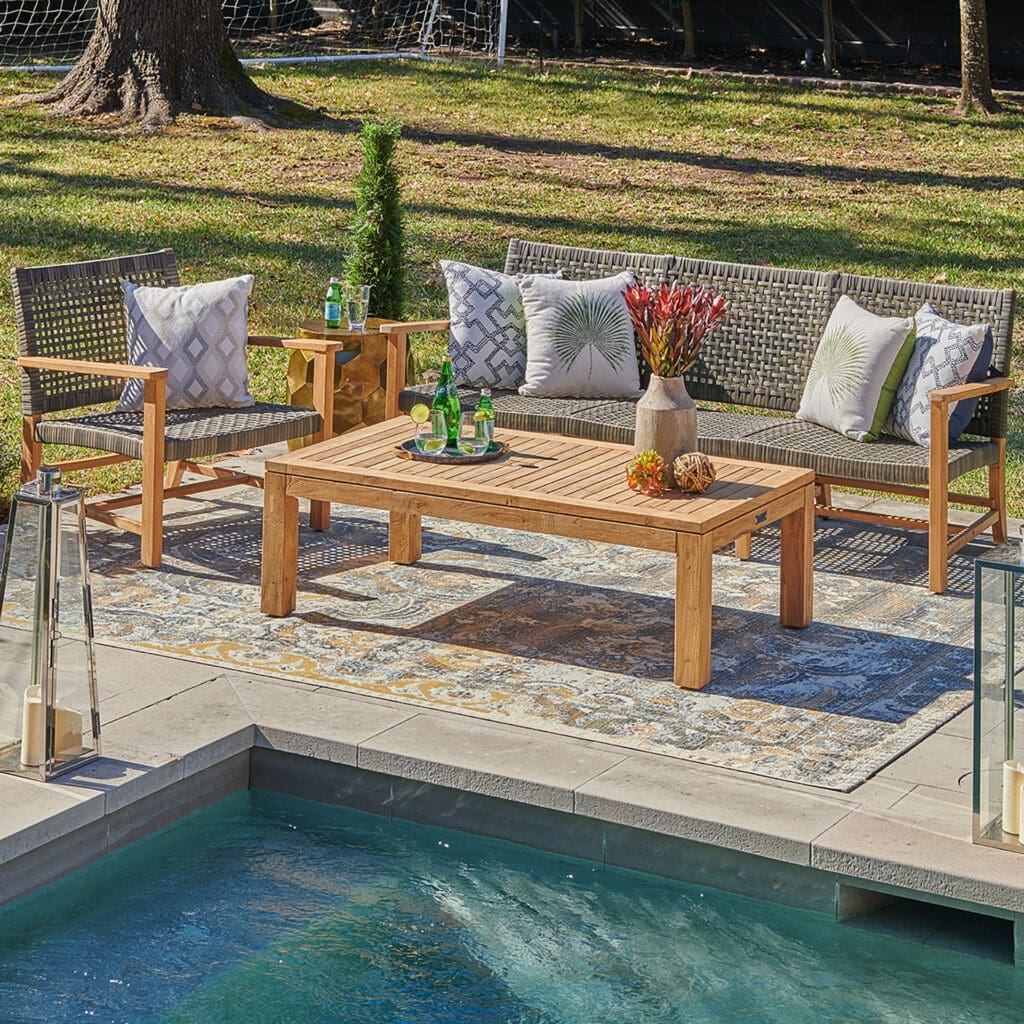 Cozy outdoor seating area with two chairs and a sofa, decorated with cushions, a wooden coffee table, and a small pool nearby.