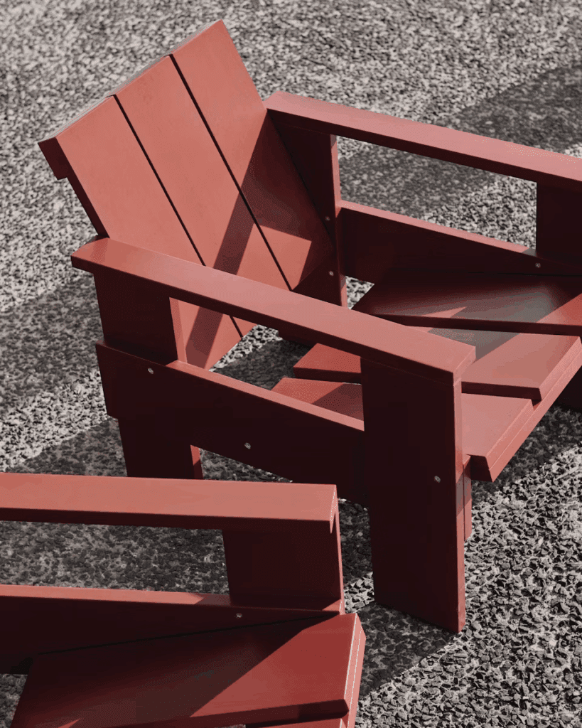 Red wooden Adirondack chairs placed on a gravel surface, showcasing their modern and minimalist design.