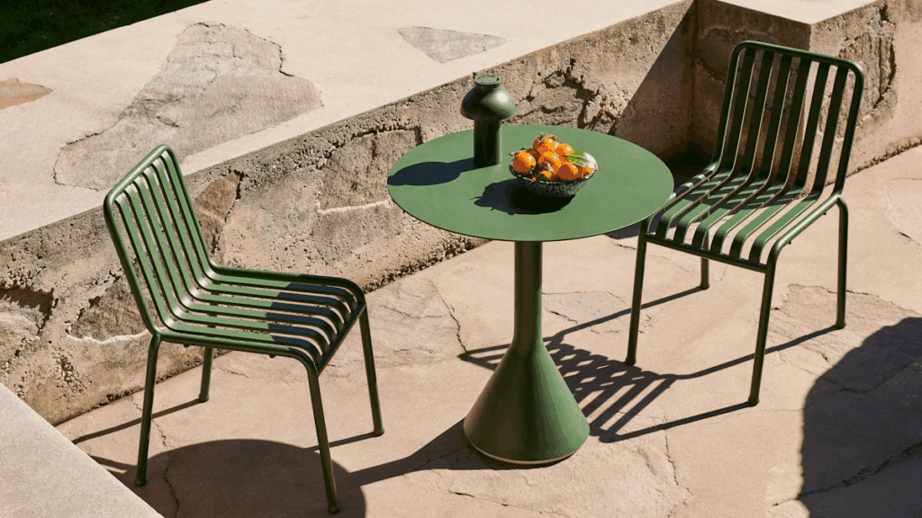 Green outdoor chairs and a round table with a bowl of oranges, set on a stone patio.
