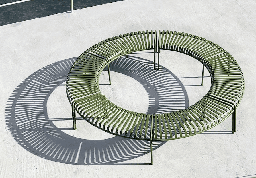 Circular green outdoor bench casting unique shadows on a concrete surface.