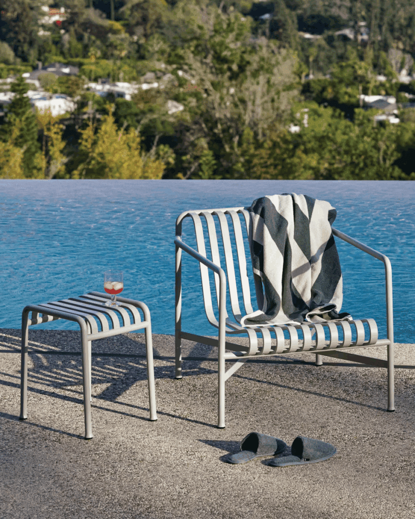 Modern outdoor seating area featuring a striped lounge chair and side table, with a swimming pool and lush greenery in the background.