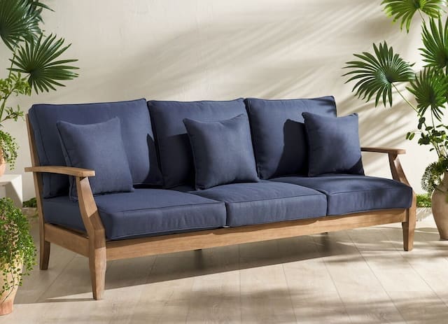 Modern outdoor sofa with navy blue cushions and a wooden frame, surrounded by potted plants.