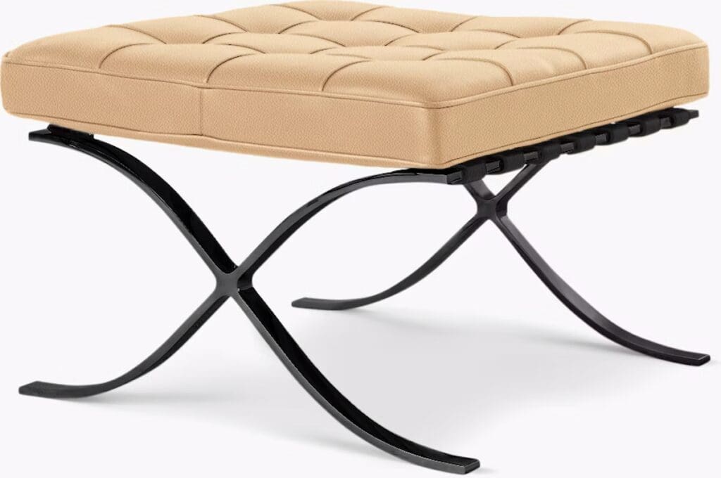 A stylish stool with a tufted beige cushion on an elegant black metal x-frame base.