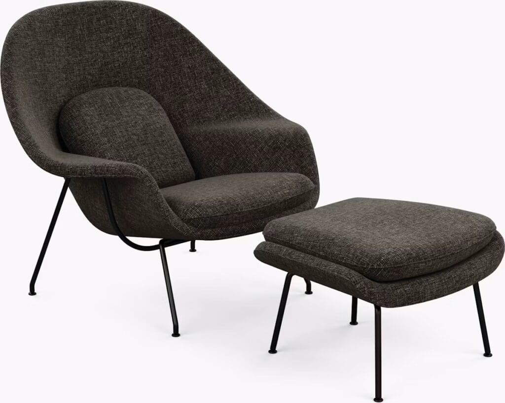 A modern armchair with a matching ottoman, both featuring a dark fabric upholstery and slender black metal legs.