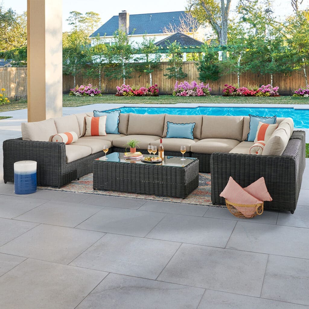 Luxurious outdoor seating area with a sectional sofa and coffee table, surrounded by greenery and a sparkling pool, ideal for relaxation and entertaining.