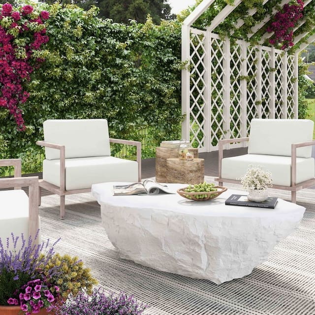 Stylish outdoor seating area featuring two white armchairs and a unique white stone coffee table, surrounded by lush greenery and flowering vines.