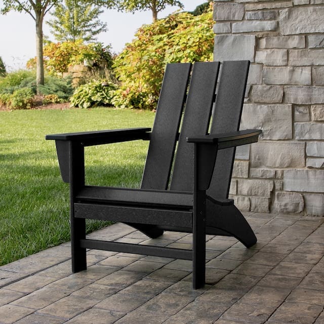 Black Adirondack chair on a stone patio with a lush garden backdrop.