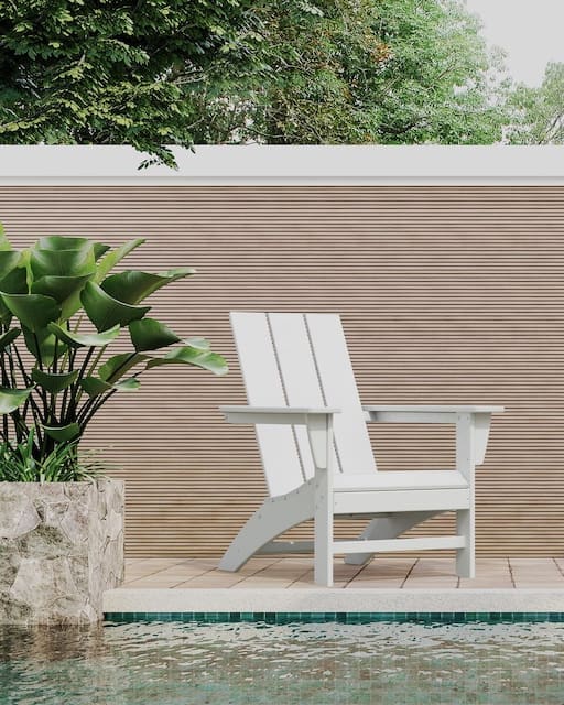 Modern outdoor space featuring an Adirondack chair beside a swimming pool, surrounded by lush greenery and a stylish stone wall.