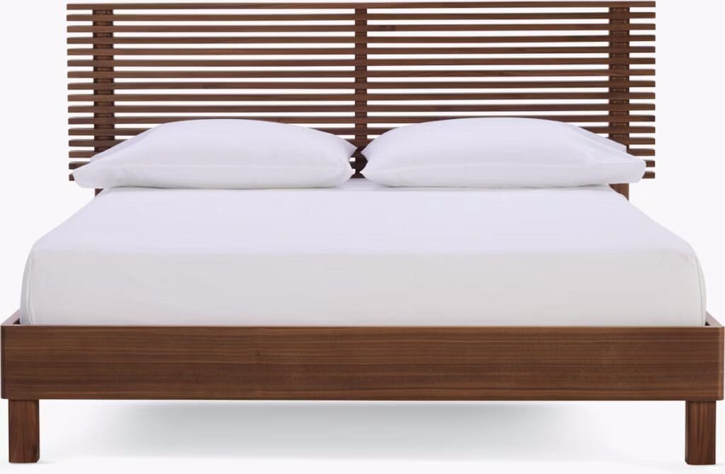 A modern wooden bed frame with a slatted headboard and white bedding, viewed from the foot of the bed.